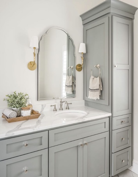 A sage-green inset vanity with a marble top and a matching floor-to-ceiling linen tower